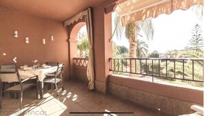Un coin repas avec une table dressée pour quatre personnes, une fenêtre donnant sur des palmiers et un balcon doté d’une rambarde en métal.