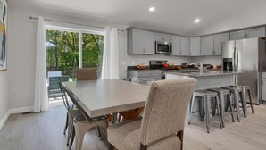 A modern kitchen with grey cabinets, stainless steel appliances, and a dining area with a table and chairs. - Modern Home on Sand Point! 11 mins to DT caseville (Caseville)