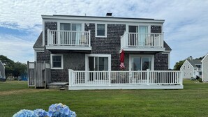 Ein zweistöckiges Haus mit einem weißen Balkon, einem rot-weiß karierten Sonnenschirm und einer Flagge.