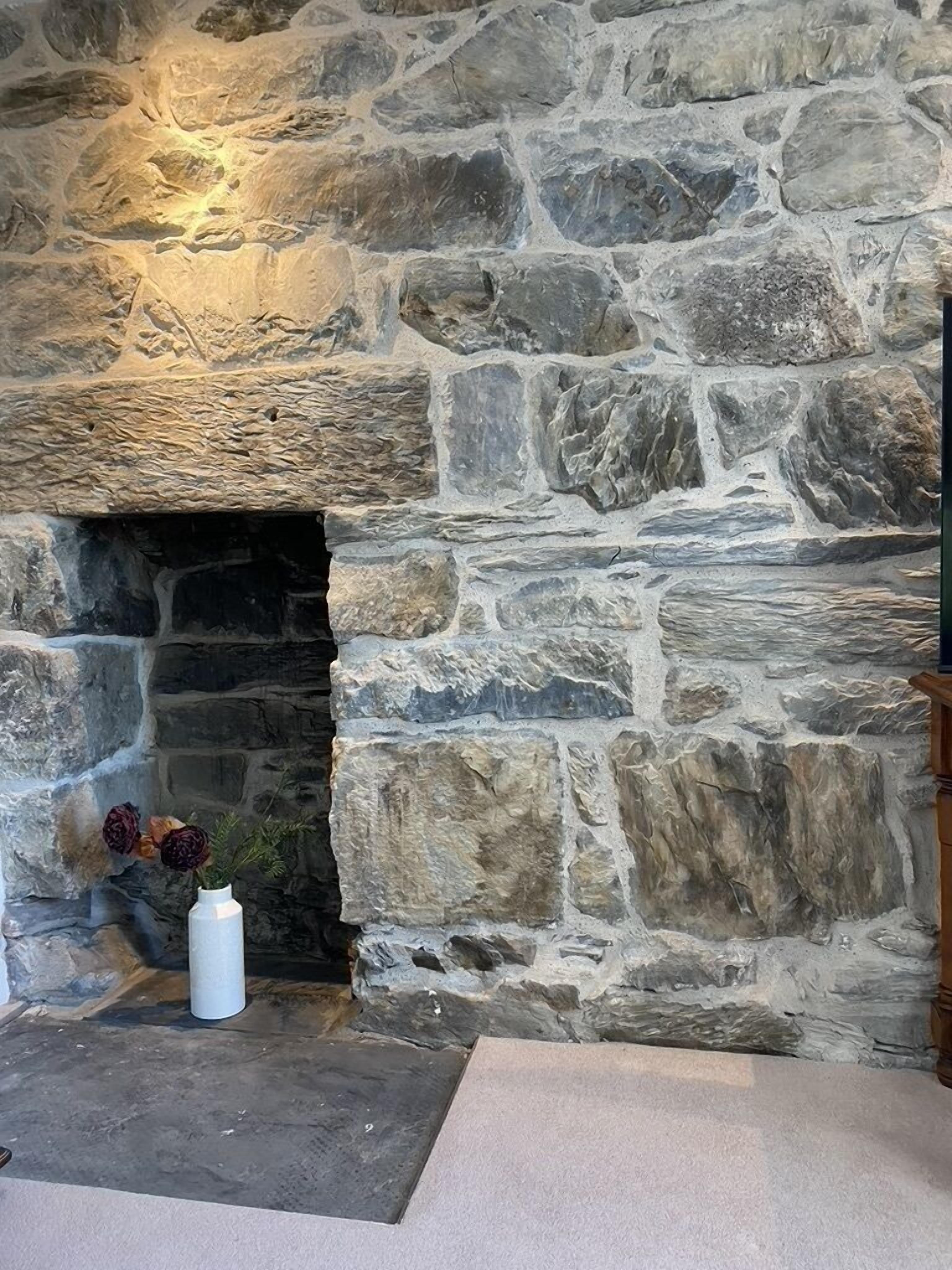 Ein Kamin aus Stein mit einer weißen Blumenvase auf der linken Seite.