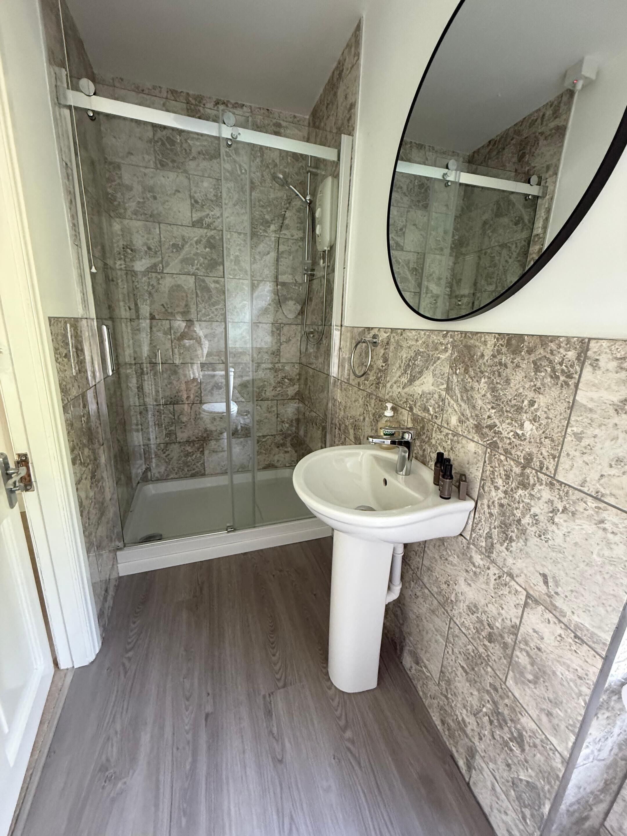 A bathroom with a glass-enclosed shower, a pedestal sink, and a large mirror.