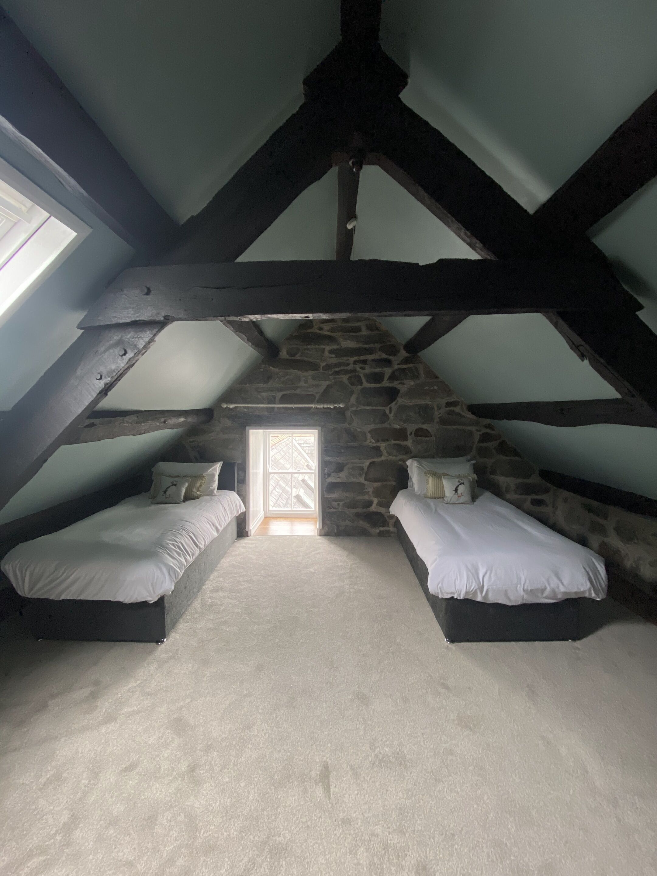 A bedroom with two beds, a stone wall, and a skylight.