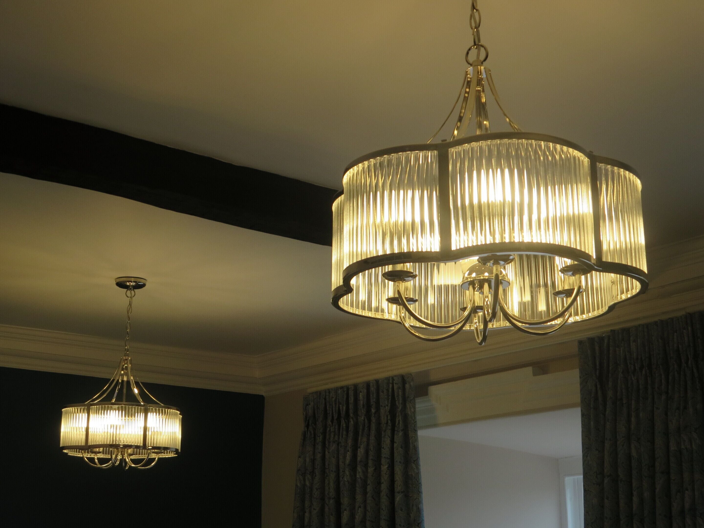 Two chandeliers in a room with dark walls and a window with curtains.