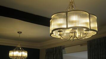 Two chandeliers in a room with dark walls and a window with curtains.