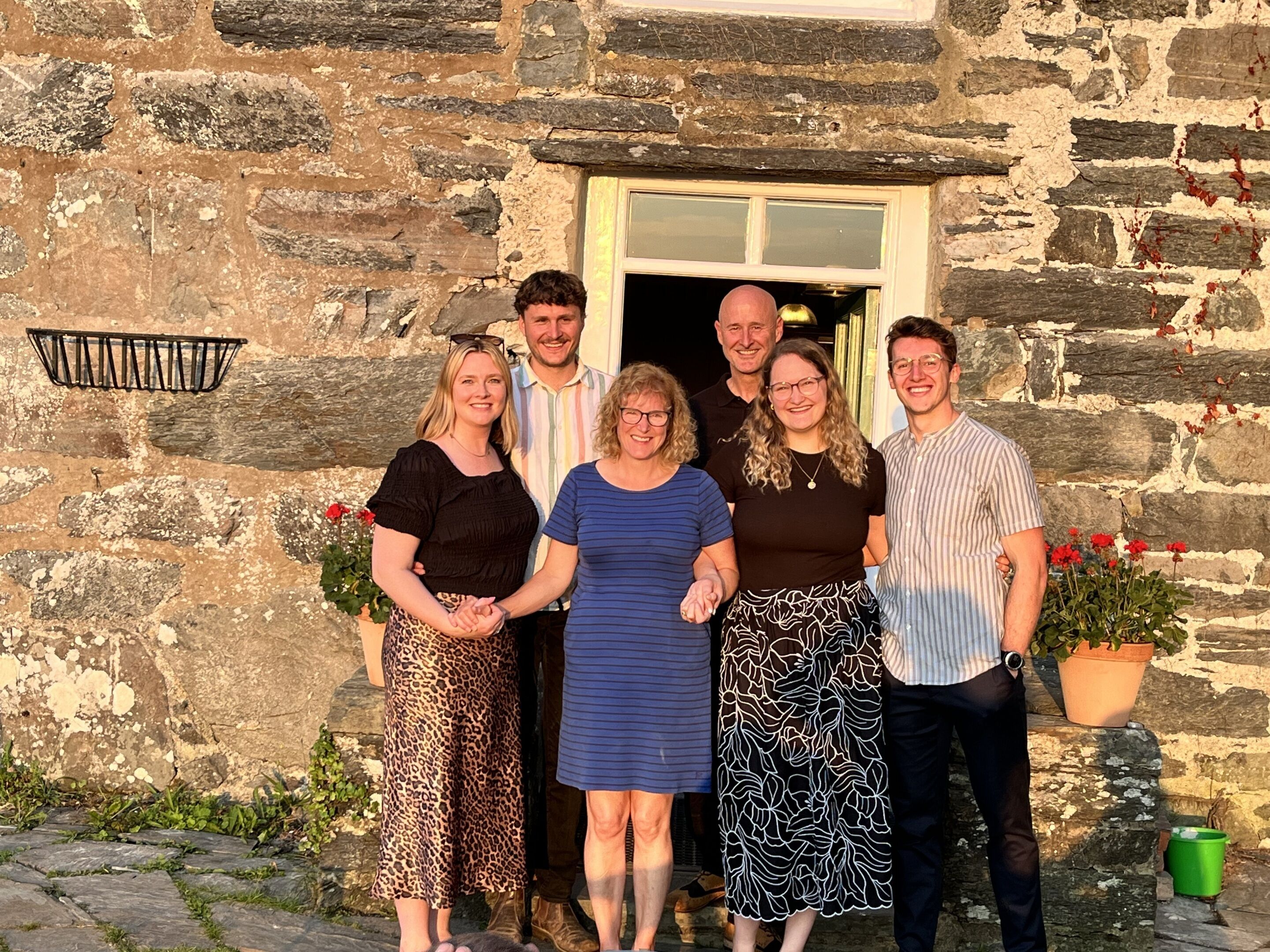 A group of people standing in front of a stone building with a window and a door.