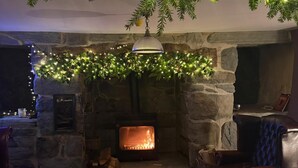 A cozy fireplace area with a stone fireplace, a plaid rug, leather seating, and festive greenery overhead. - Maes Y Neuadd Country House (Talsarnau)