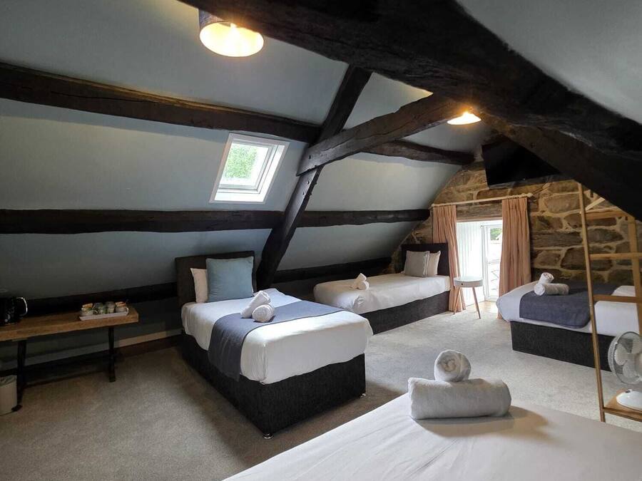 A cozy attic bedroom with three beds, a wooden ladder, and a stone wall.