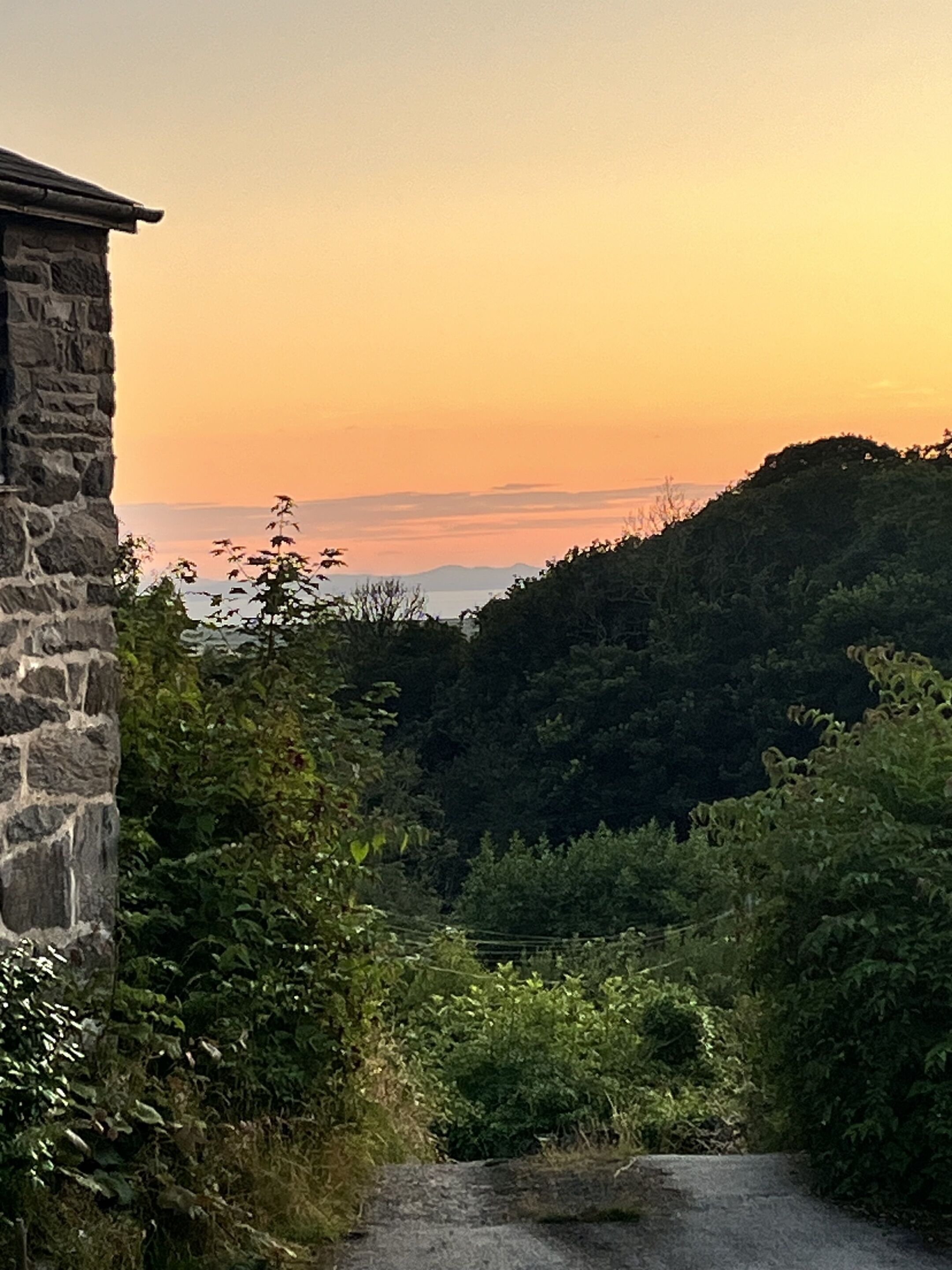 A stone building with a view of a sunset over a forested hill.