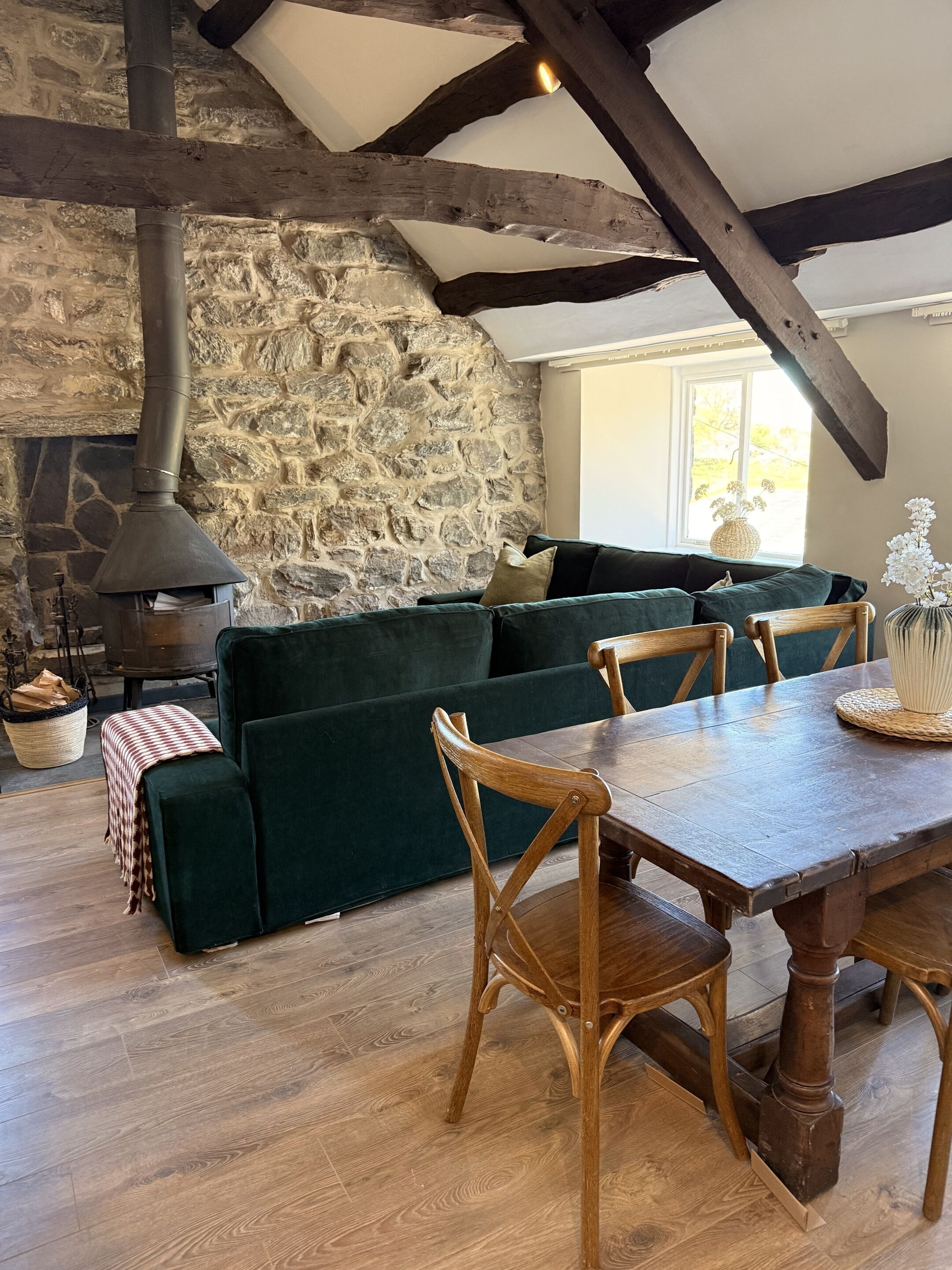 Una habitación acogedora con pared de piedra, sofá verde, sillas de madera y una mesa.