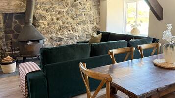 Una habitación acogedora con pared de piedra, sofá verde, sillas de madera y una mesa.