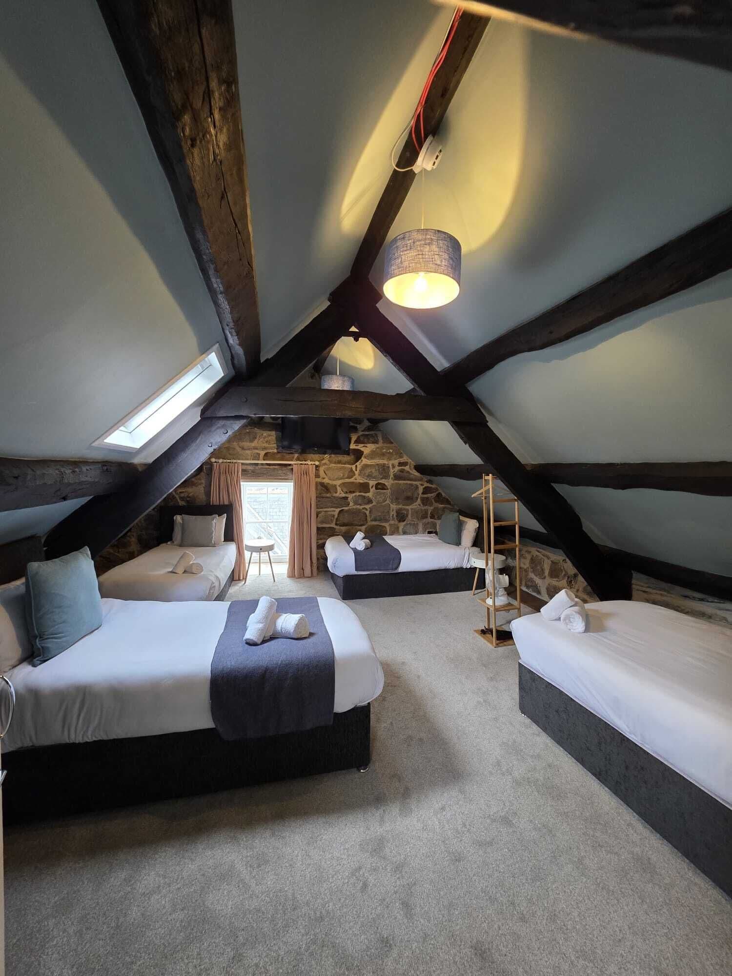 A cozy attic bedroom with three beds, a stone wall, and a skylight.