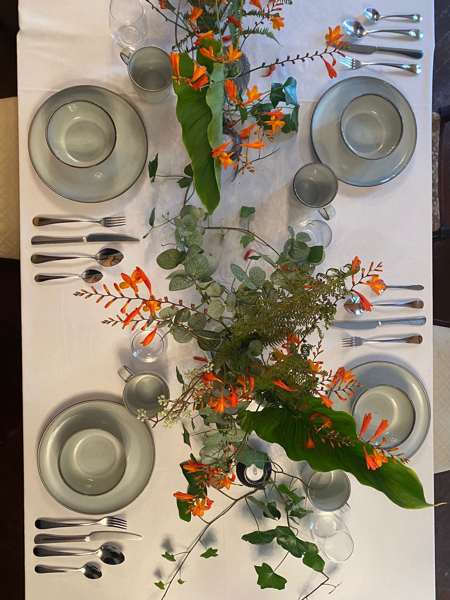 A table set with plates, cutlery, and a centerpiece of flowers and greenery.