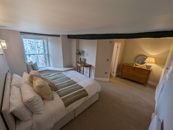 Quarto com uma cama grande, cômoda de madeira, mesa de cabeceira e janela com vista para um edifício de pedra.