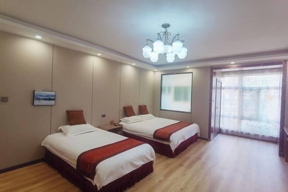 Habitación de hotel con dos camas, un ventanal con vistas, un candelabro y una pantalla de proyector.