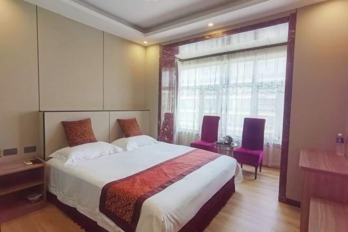 Una habitación de hotel con una cama grande, una mesita, una silla y una ventana con cortinas.