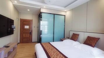 A hotel room with a large bed, a flat-screen TV mounted on the wall, a wooden bench, and a sliding glass door closet.