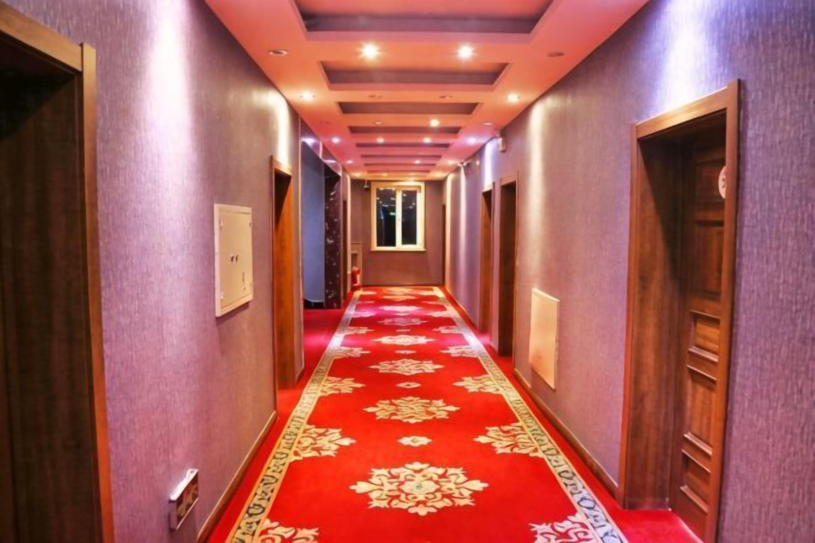 A hotel hallway with a red carpet, wooden doors, and a ceiling with recessed lighting.