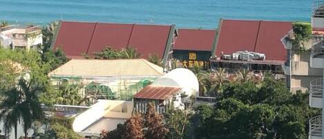 A coastal building with a red roof, a white dome structure, and a flat-roofed building with a green roof.