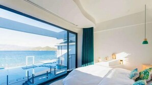 Een moderne hotelkamer met een groot bed, uitzicht op zee en een balkon met zitplaatsen.
