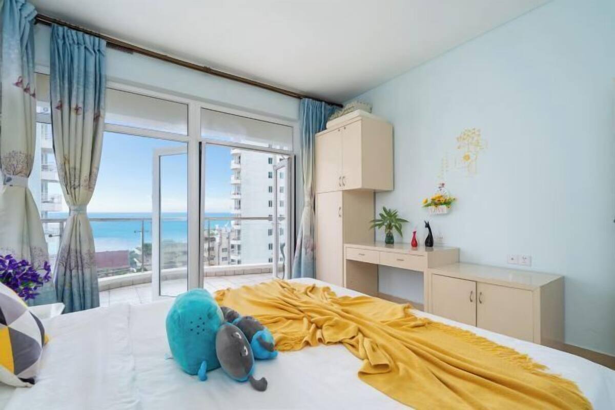 Une chambre d’hôtel avec un lit, une armoire, un bureau, une plante et une vue sur la mer.