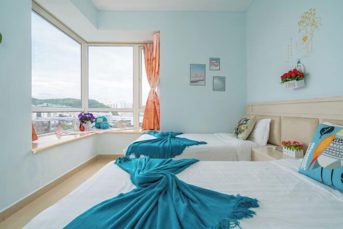 A hotel room with two beds, a large window with curtains, a view of the city, and a wall with decorative items.