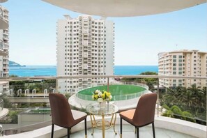A balcony with a round table and two chairs, overlooking a cityscape and the sea. - Sanya Hai Hua Apartment (Sanya)