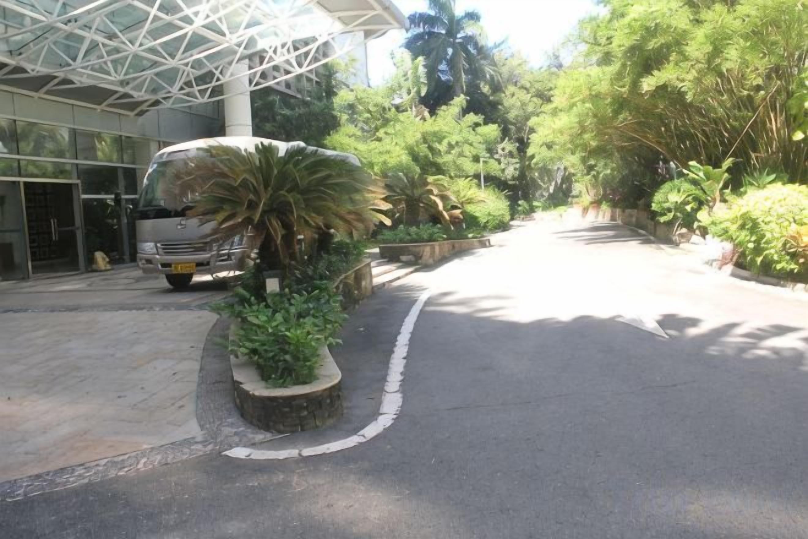 A parking area with a vehicle, a building entrance, and surrounding greenery.