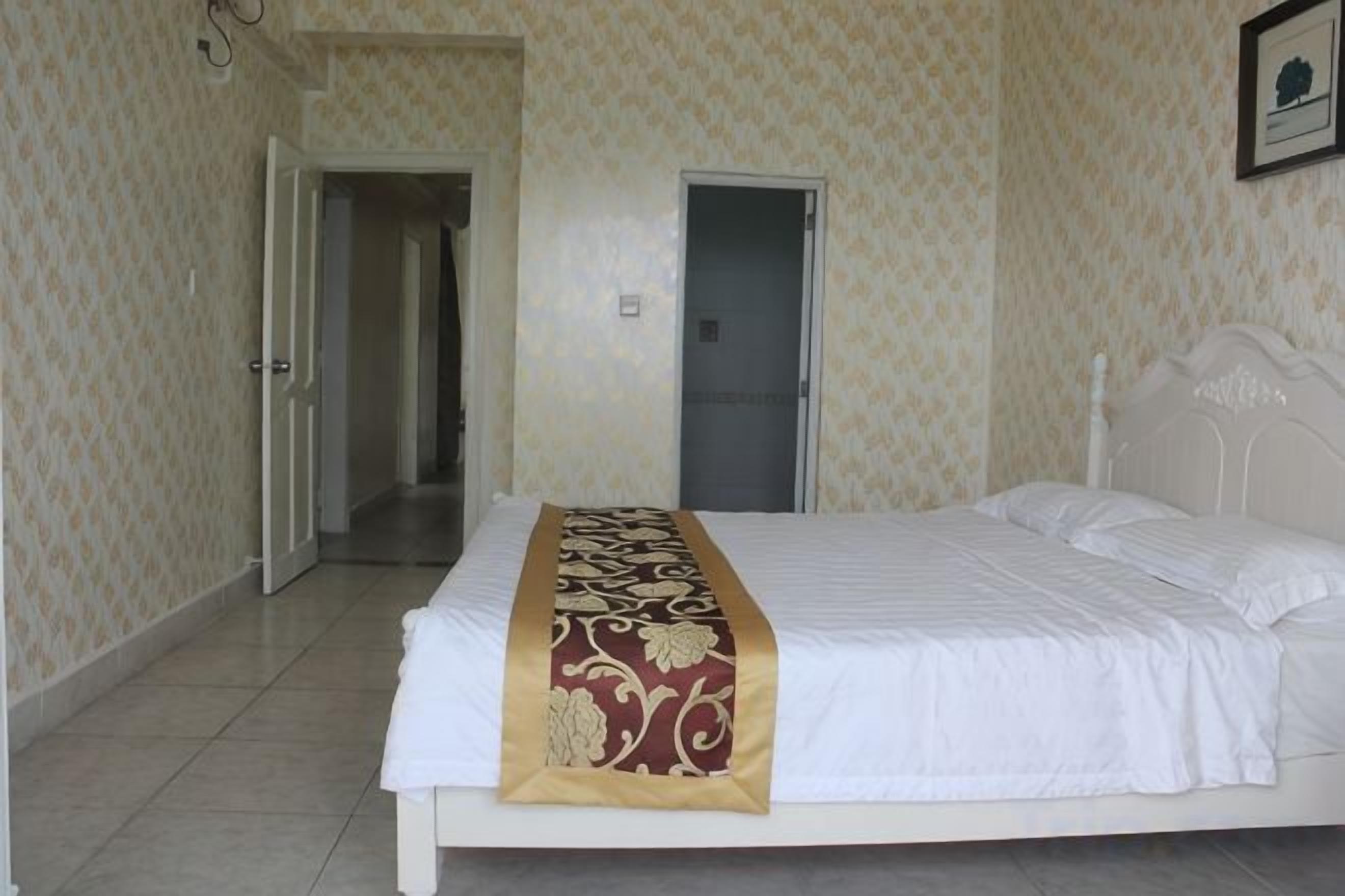 A hotel room with a bed, a door, and a wall with a patterned wallpaper.