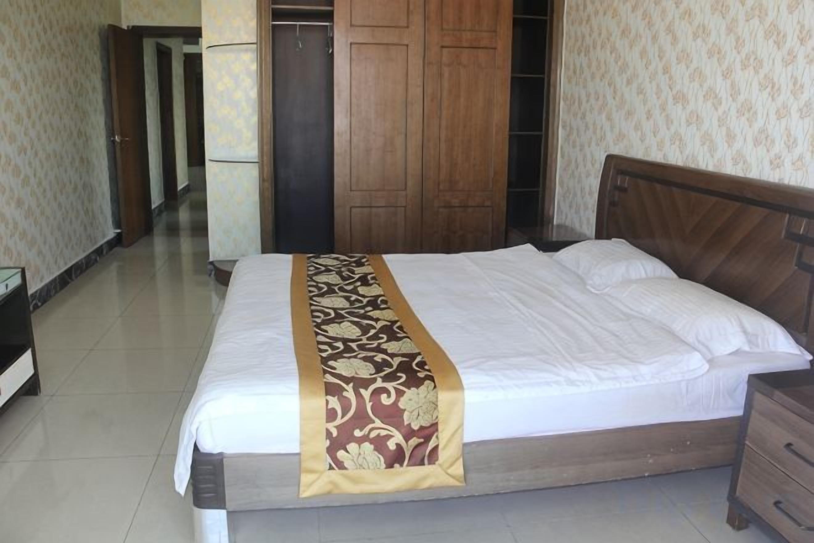 A neatly made bed with a decorative bedspread, a wooden headboard, and a bedside table with drawers.