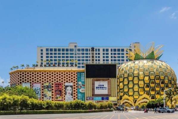 A building with a pineapple sculpture in front, a large blue and white structure in the background, and various signs and advertisements on the building facade.