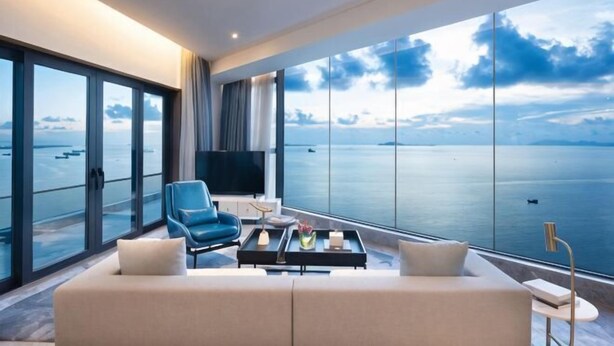 Een moderne hotelkamer met een groot raam met uitzicht op de zee, een bank, een stoel en een salontafel.