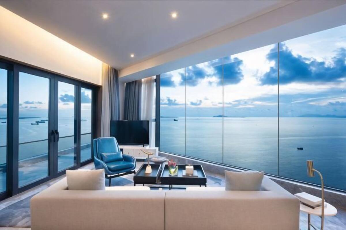 Une chambre d’hôtel moderne dotée d’une grande fenêtre donnant sur la mer, d’un canapé, d’un fauteuil et d’une table basse.