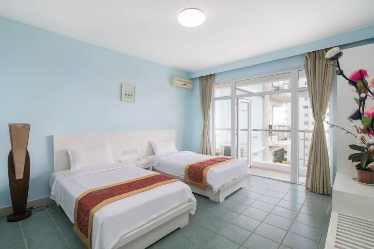 Une chambre d’hôtel avec deux lits, une grande fenêtre et une plante en pot.