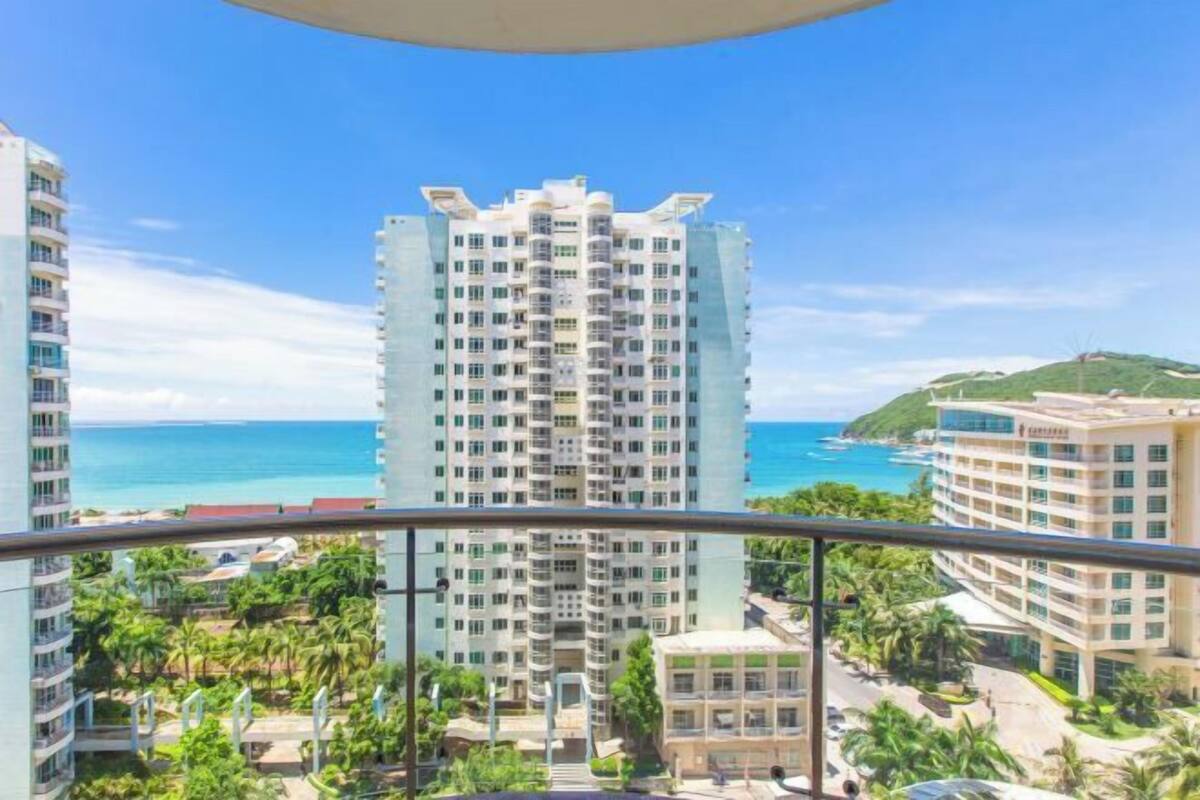 Un hôtel de grande hauteur, avec de nombreux étages, offrant une vue sur l’océan et s’intégrant dans un paysage tropical agrémenté de palmiers.