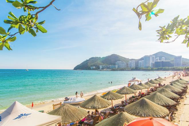 Una spiaggia con ombrelloni di paglia e una vista limpida sull'oceano, con una montagna sullo sfondo.