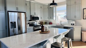 A modern kitchen with grey cabinets, stainless steel appliances, a marble island, and pendant lighting. - 3 mins drive to Beach |5 bdrm|Sleeps 18 (Port Elgin)