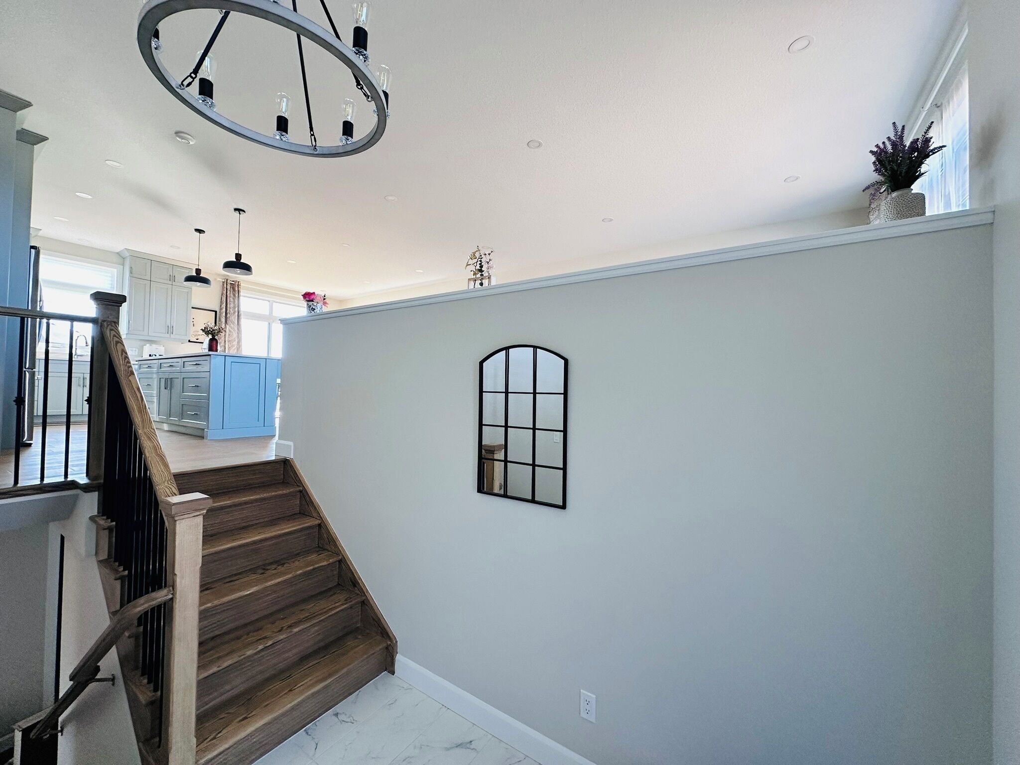 A spacious interior with a wooden staircase, a kitchen area in the background, and a large window on the upper floor.
