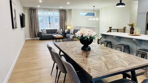 A modern living room with a sofa, a dining table with chairs, and a kitchen area with a counter and stools. - 3 mins drive to Beach |5 bdrm|Sleeps 18 (Port Elgin)