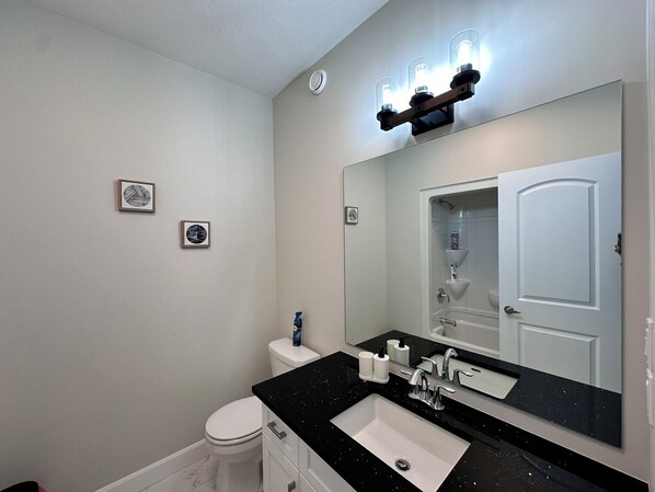 Un baño moderno con lavamanos de superficie negra, un espejo grande y un inodoro. Hay dos cuadros enmarcados en la pared.