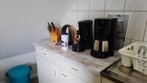 A kitchen with a white countertop, coffee makers, a knife block, and a trash bin. - Neue und Ruhig Gelegene Ferienwohnung am Wittensee und in den Hüttener Bergen (Klein Wittensee)