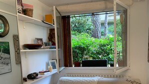 A cozy room with a corner sofa, a wooden table, and a window overlooking greenery. - Studette Meublée - Boulogne-billancourt Face au Stade de Roland-garros (Boulogne-Billancourt)