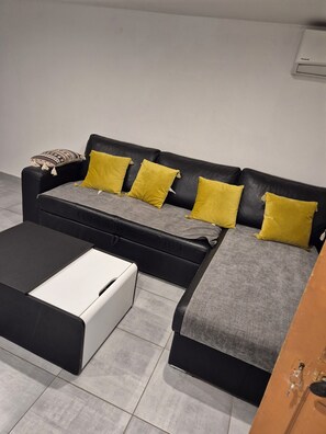 Uma sala de estar moderna com um sofá de couro preto, um banquinho cinza e preto e almofadas amarelas.