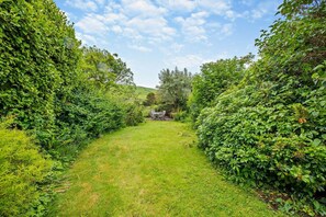 A lush garden pathway leading to a rustic outdoor seating area with a table and chairs.