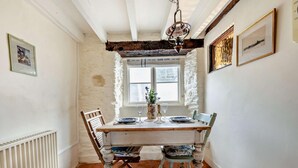 A dining room with a rustic wooden table, two chairs, a hanging light fixture, and a window with a view.