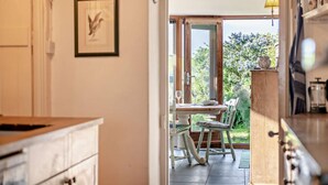 An open doorway leading to a dining area with a table and chairs, a framed picture on the wall, and a view of greenery outside.