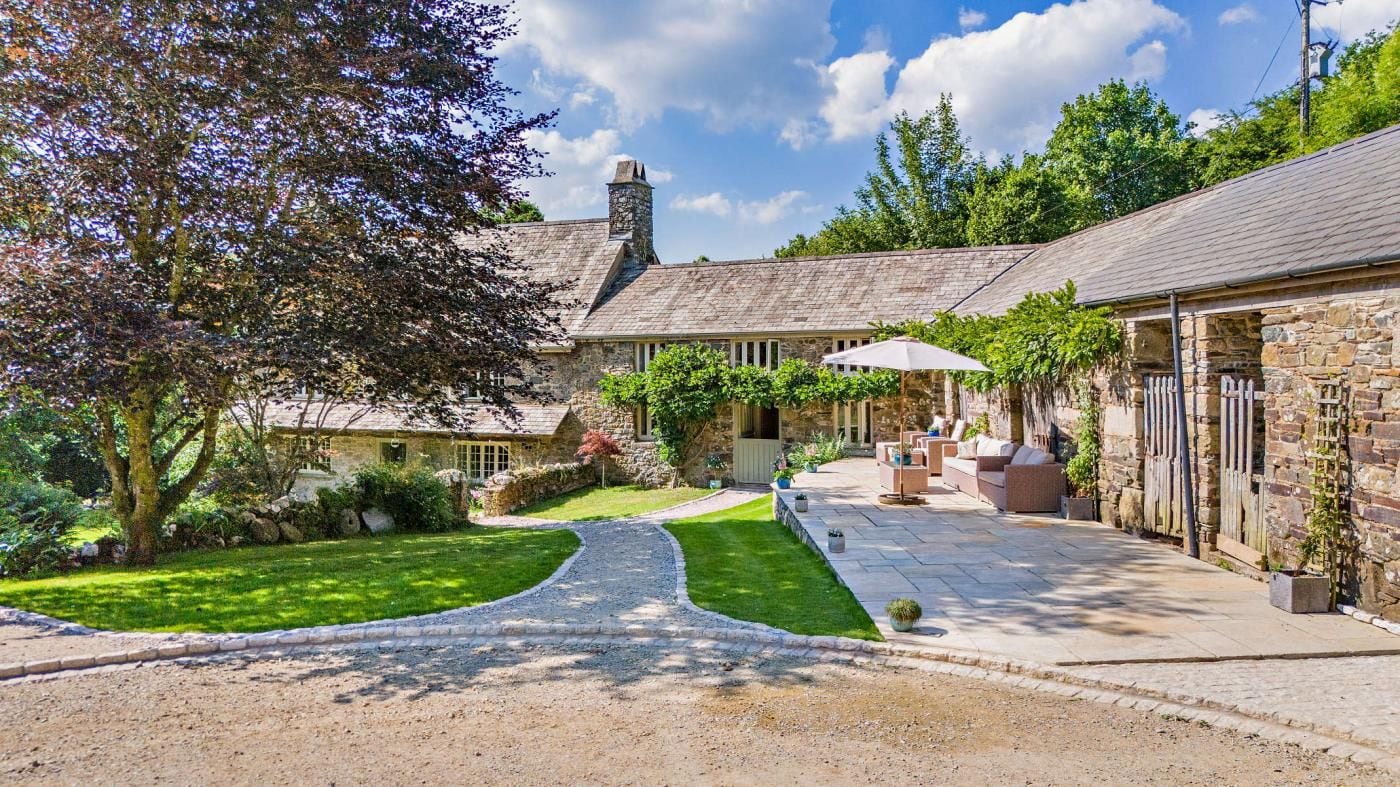 A stone building with a paved courtyard, outdoor seating, and a pathway leading to the entrance.