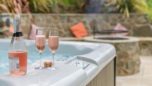 A hot tub with a bottle of pink drink and two glasses on the edge.
