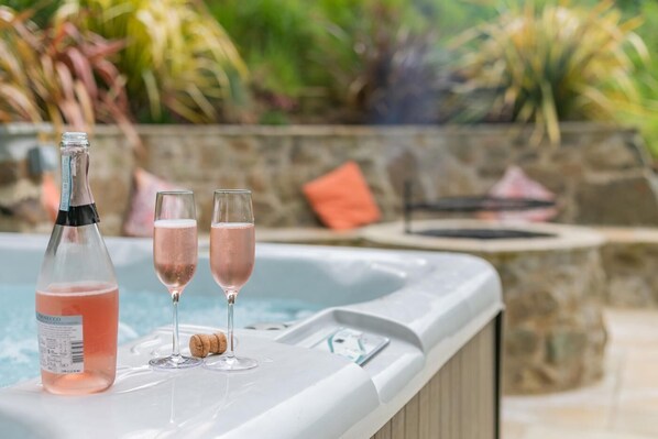 A hot tub with a bottle of pink drink and two glasses on the edge.