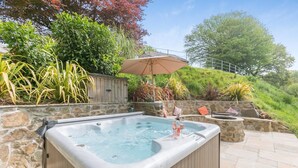 A hot tub with a stone wall backdrop, a wooden deck, and a stone staircase leading up.