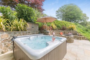 A hot tub with a stone wall backdrop, a wooden deck, and a stone staircase leading up. - 2 Bed in Kelly (oc-k29333) (Kelly)